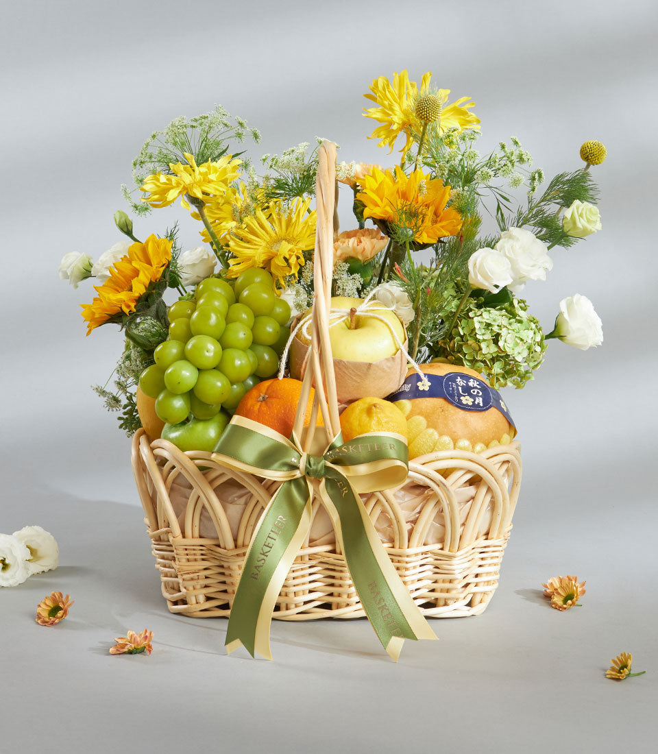 Bright yellow sunflower and fresh fruit gift basket with green apples, oranges, and white blooms in woven wicker