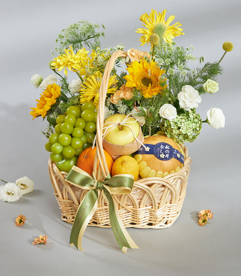Bright yellow fruit and floral gift basket with sunflowers, roses, fresh citrus, and grapes in woven wicker