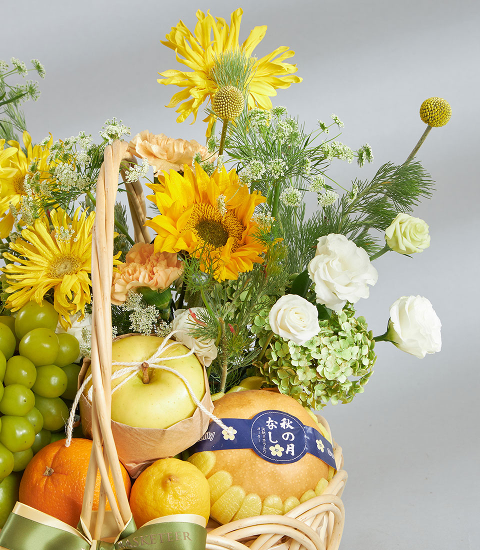 Bright yellow and white flowers with fresh citrus, apples, and pears in a woven gift basket