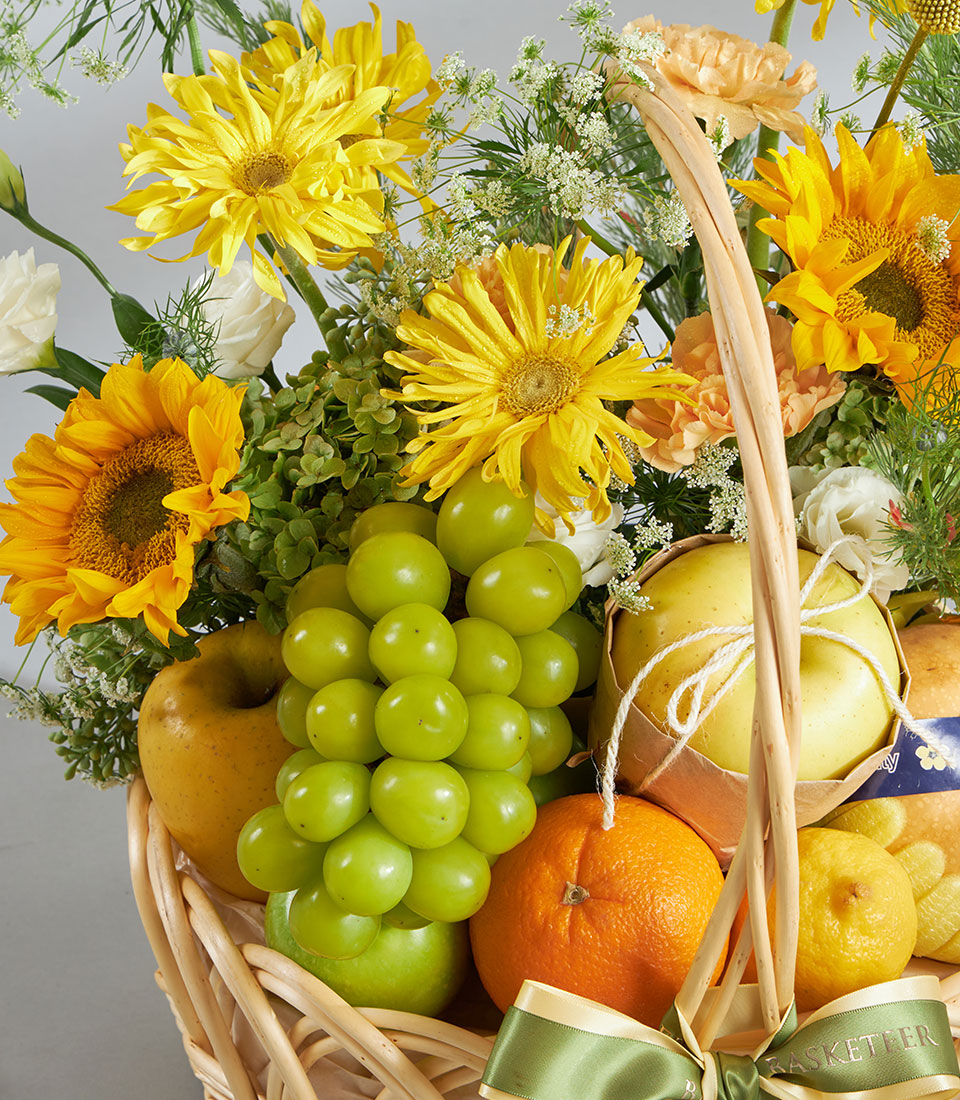Bright yellow fruit and flower gift basket with sunflowers, apples, grapes, and fresh citrus in woven wicker