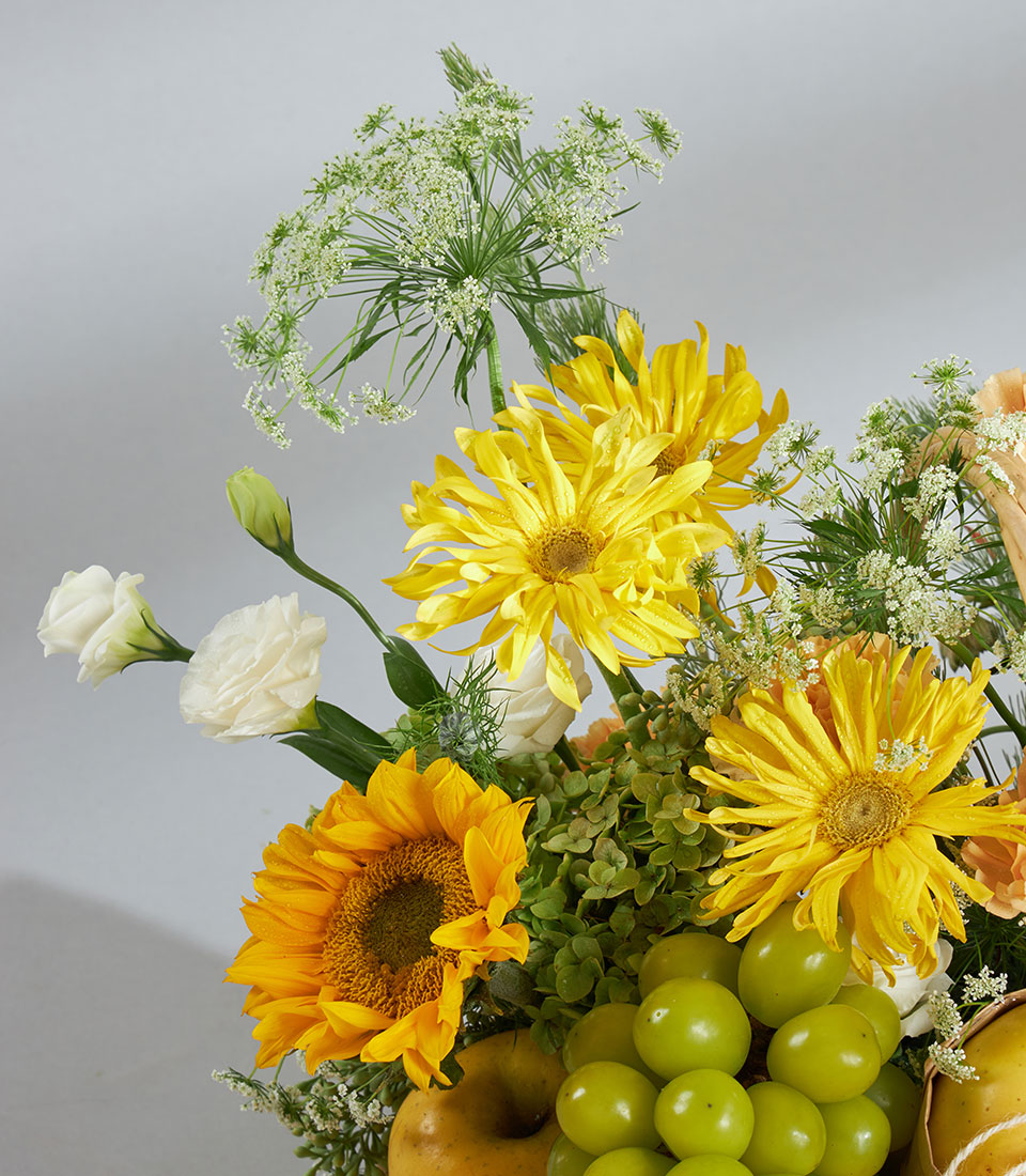 Bright yellow sunflowers and daisies with fresh green grapes and pears in premium fruit and flower gift basket