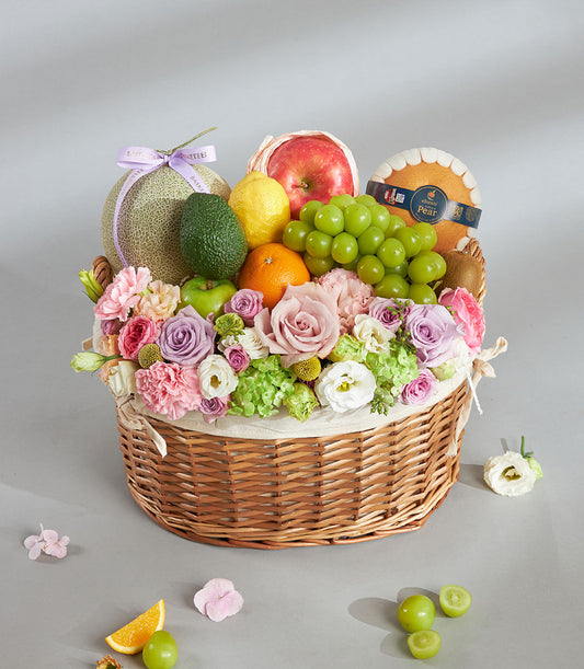 Pastel fruit and flower birthday basket with fresh melons, apples, citrus, and roses in woven wicker