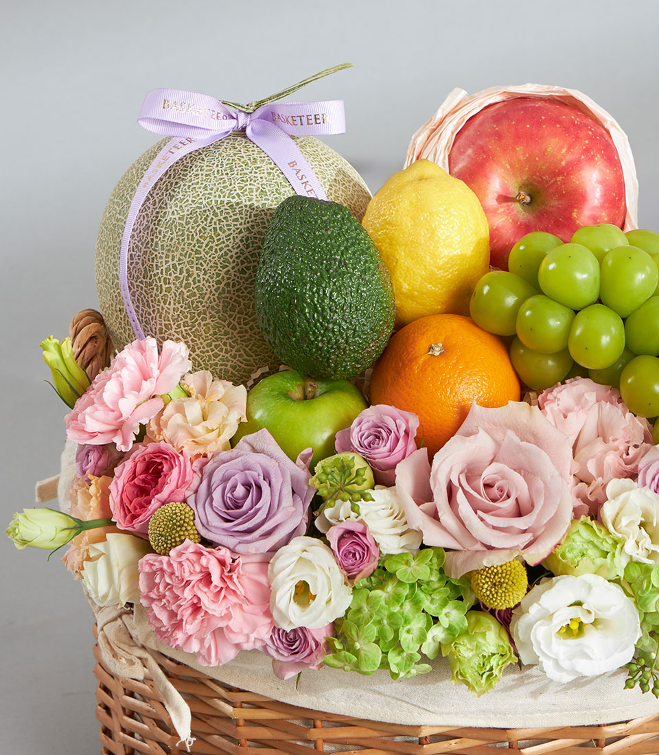 Pastel fruit and floral birthday basket with cantaloupe, grapes, roses, and carnations in woven wicker