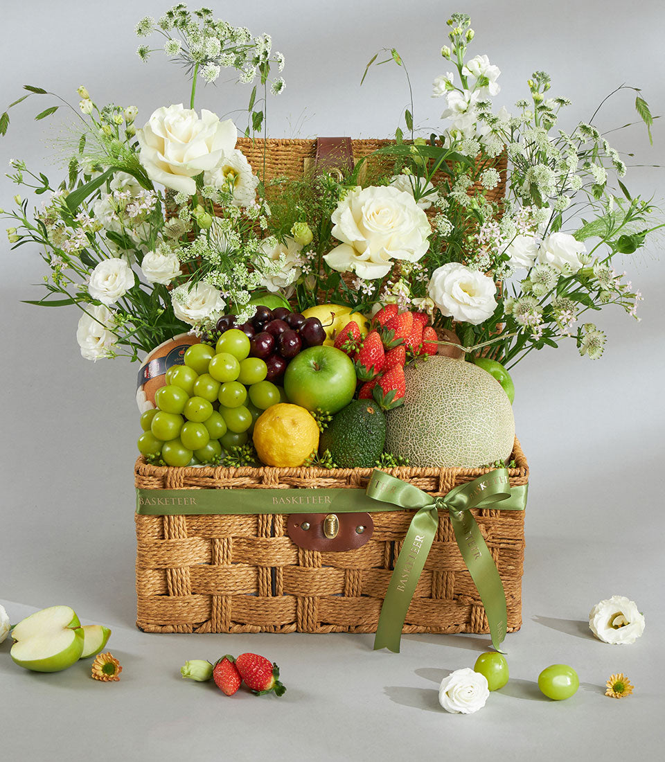 Premium wicker fruit and flower gift basket with white roses, fresh grapes, strawberries, and apples
