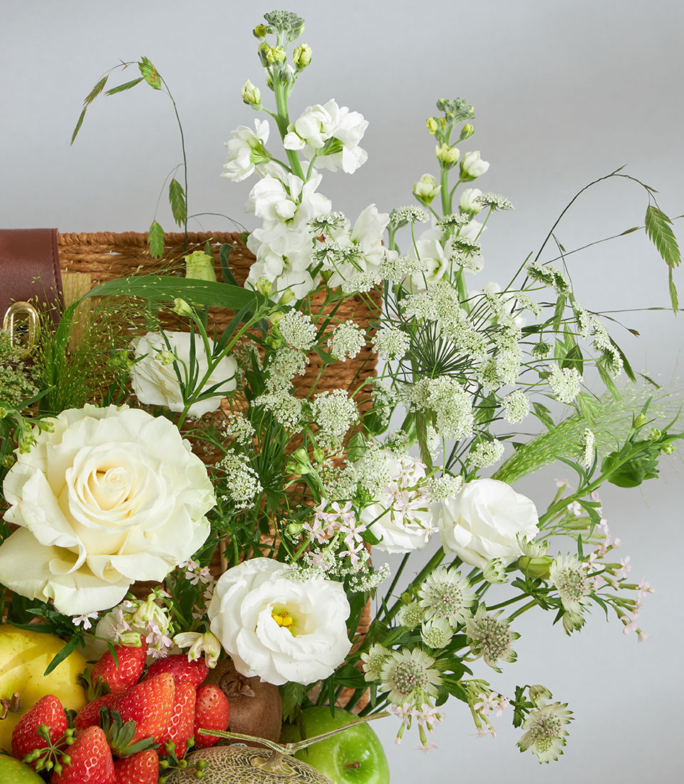 White roses and fresh fruit in woven wicker gift basket with leather handle