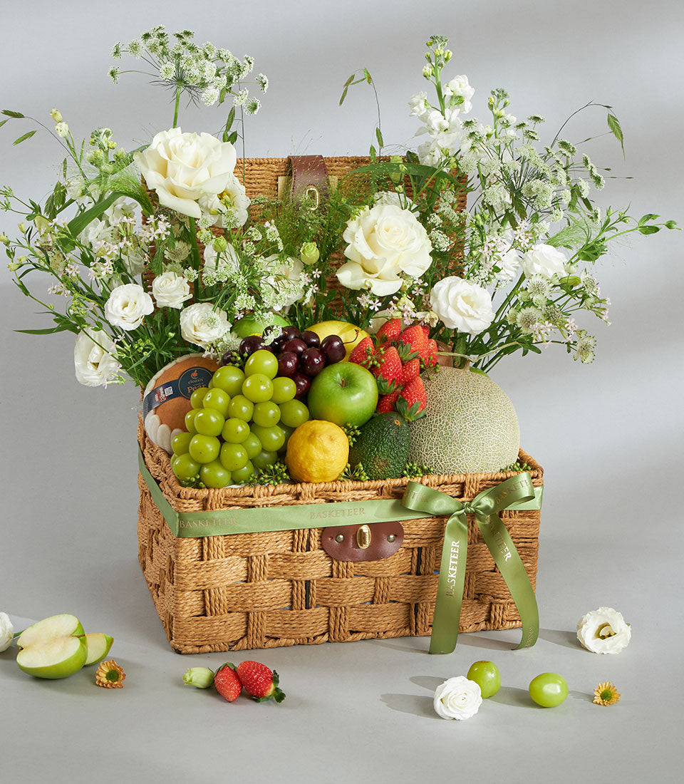 Woven natural fiber basket with fresh fruit, white roses, and green ribbon—premium gift hamper for elegant occasions