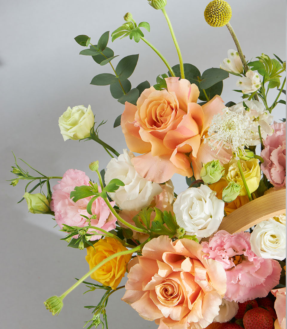 Premium fruit and floral birthday basket with peach roses, lisianthus, ranunculus, and fresh strawberries in wooden container