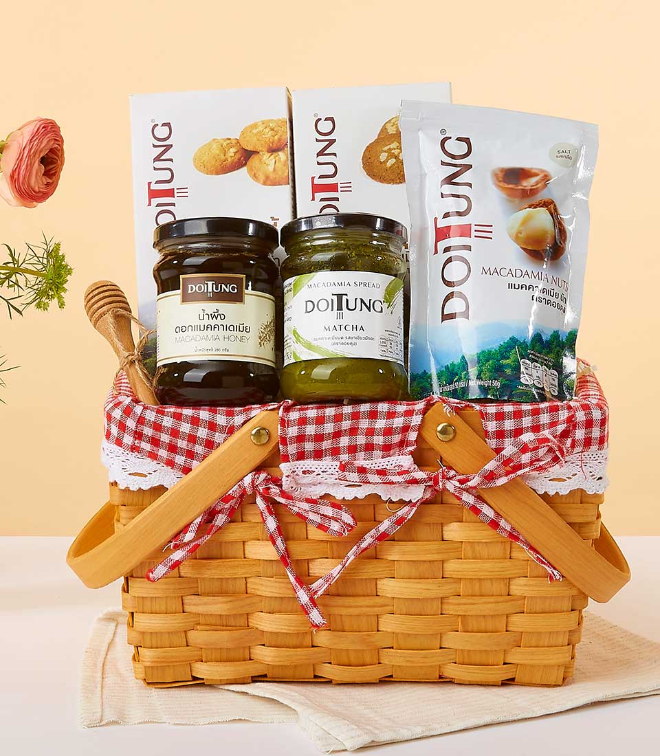 Light brown woven basket with wooden handles lined in red gingham, filled with macadamia honey, matcha spread, cookies, and
