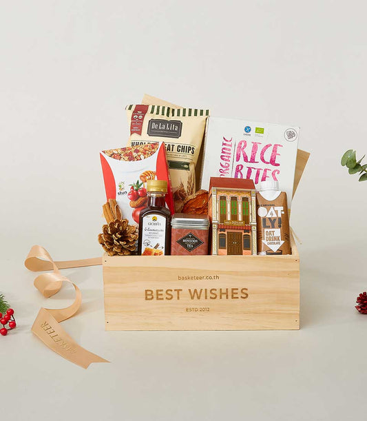 Wholesome Worldly Wonders gift box with gourmet snacks, tea, chocolate oat drink, and festive botanical accents in wooden