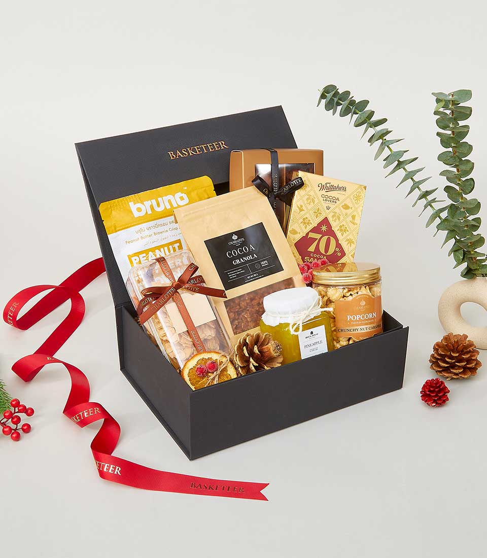 Luxe black gourmet gift box with brownie crisps, granola, caramel popcorn, and jam, finished with red ribbon for New Year