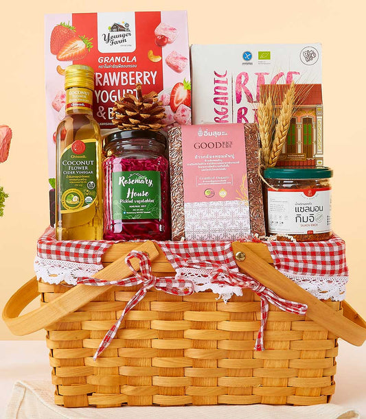 Woven wicker gift basket with red gingham lining filled with organic foods, wellness ingredients, and artisan pantry