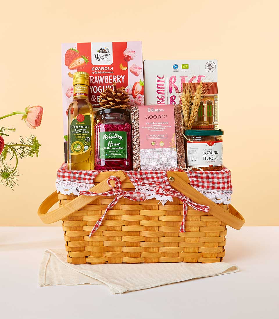 Woven picnic basket with gingham lining filled with premium wellness foods including granola, cider vinegar, pickled