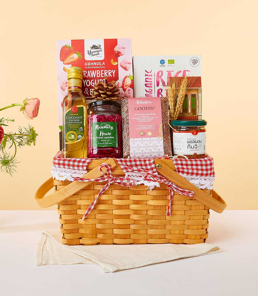 Woven picnic basket with gingham lining filled with premium wellness foods including granola, cider vinegar, pickled