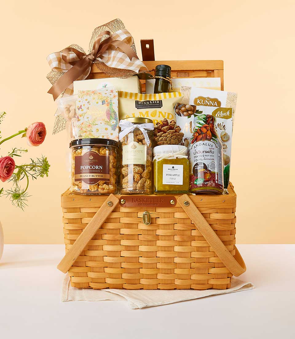 Woven picnic basket filled with gourmet wellness snacks, dates juice, and peanut butter, tied with plaid ribbon for New Year