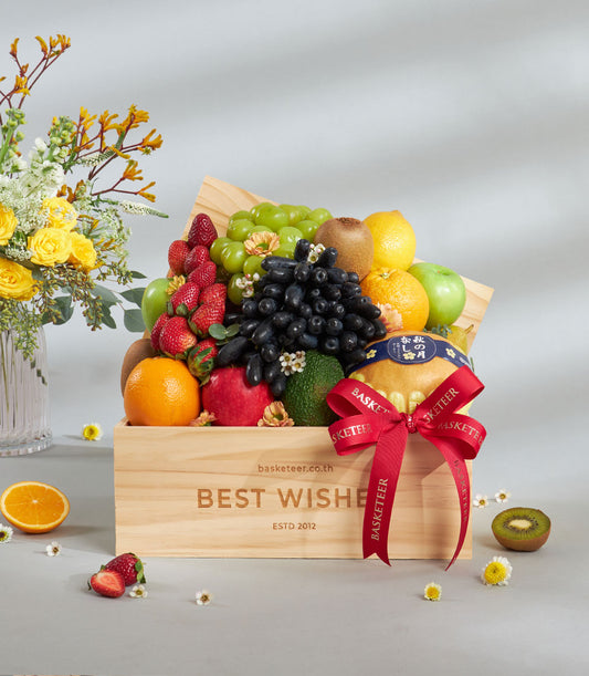 Wooden fruit crate with fresh assorted fruits, red ribbon bow, and yellow roses in glass vase