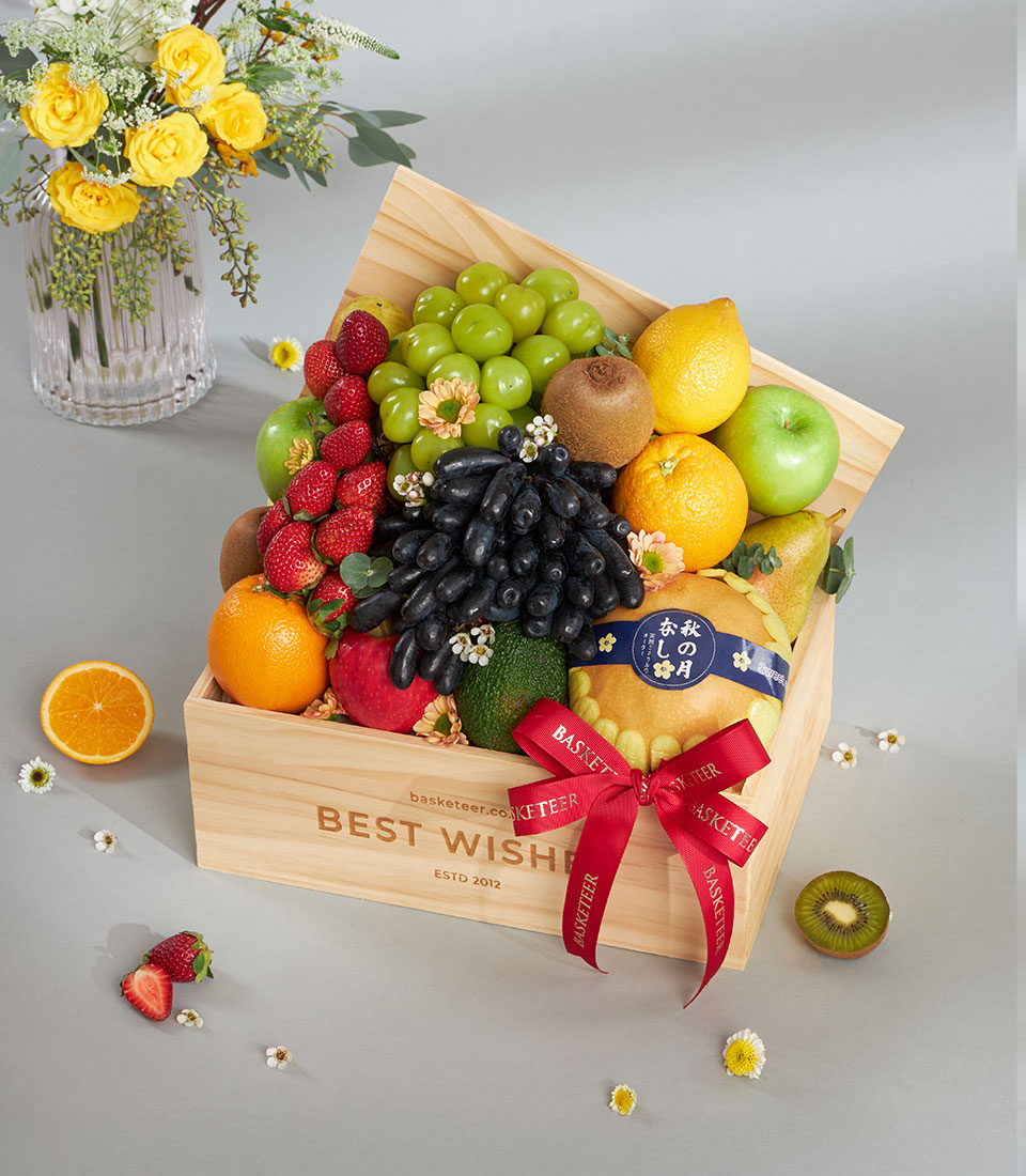 Wooden gift crate filled with fresh assorted fruits, grapes, strawberries, and citrus with red ribbon bow