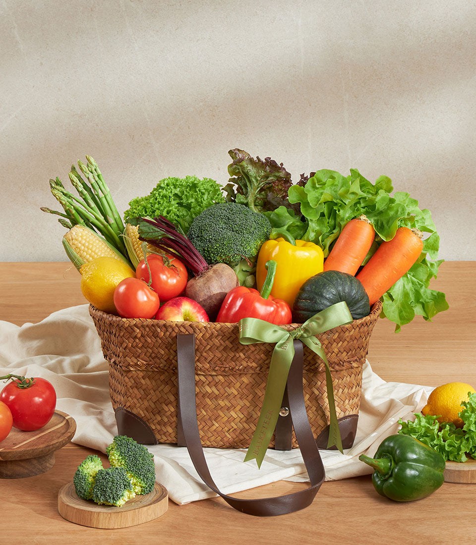 Fresh farm vegetable basket with asparagus, peppers, tomatoes, carrots, and greens in woven straw with leather handles