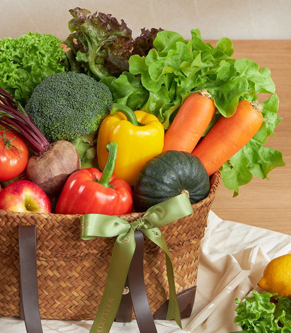 Woven straw basket filled with fresh farm vegetables and fruits, vibrant produce arrangement with green satin ribbon