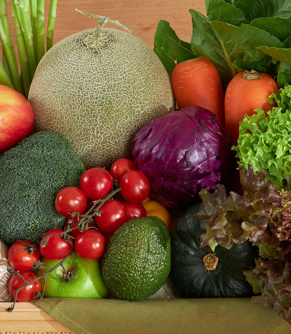 Wooden crate of fresh vegetables and fruits including broccoli, carrots, tomatoes, and avocado for health-conscious gifting