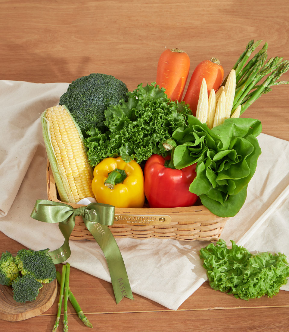 Fresh vegetable gift basket with broccoli, corn, bell peppers, and leafy greens in woven basket