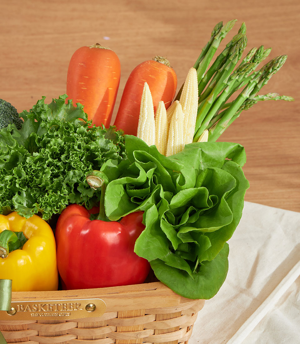 Vibrant fresh vegetable basket with carrots, asparagus, bell peppers, and leafy greens in woven wicker