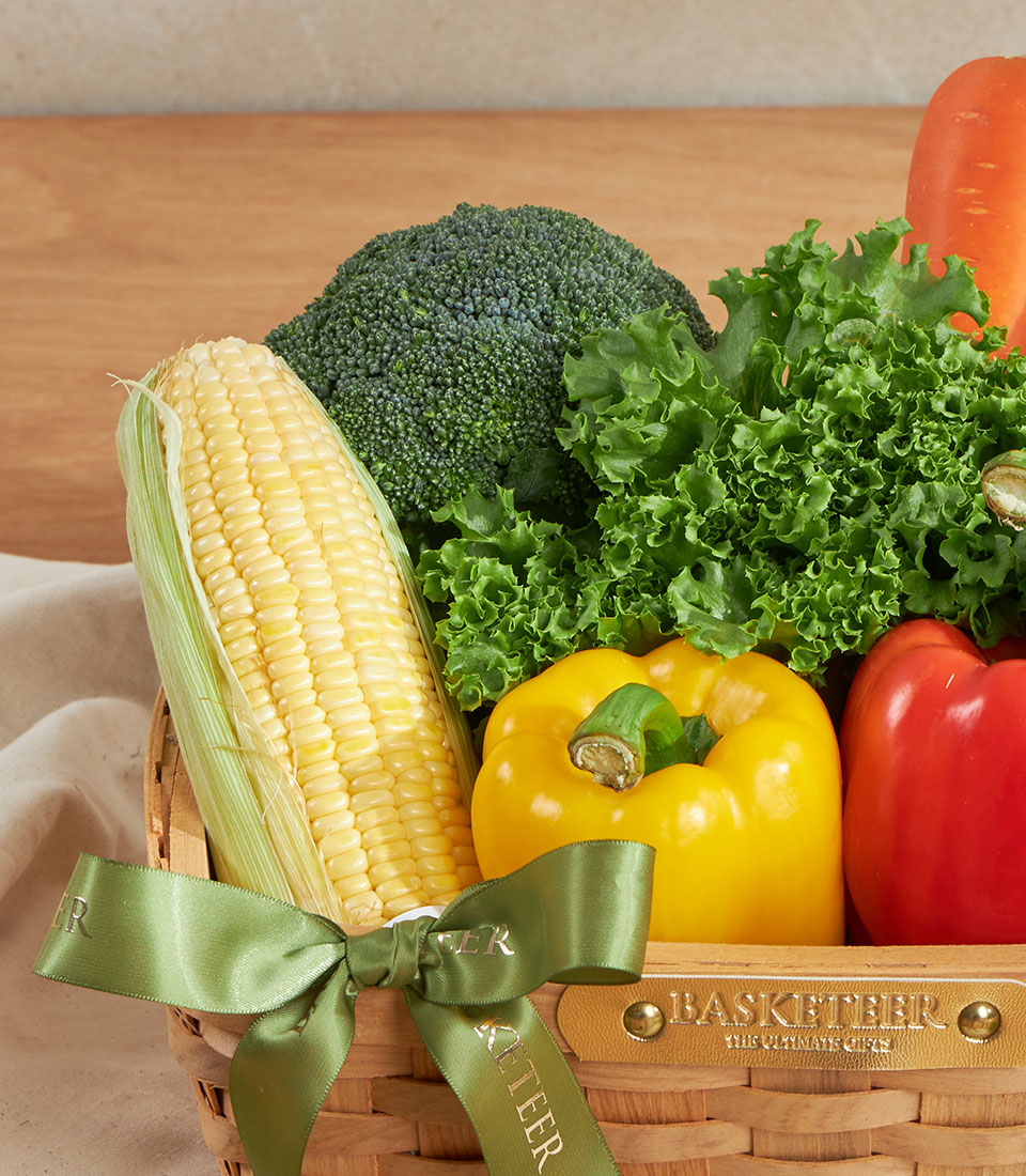 Fresh vegetable gift basket with corn, broccoli, bell peppers and lettuce in woven basket with green ribbon