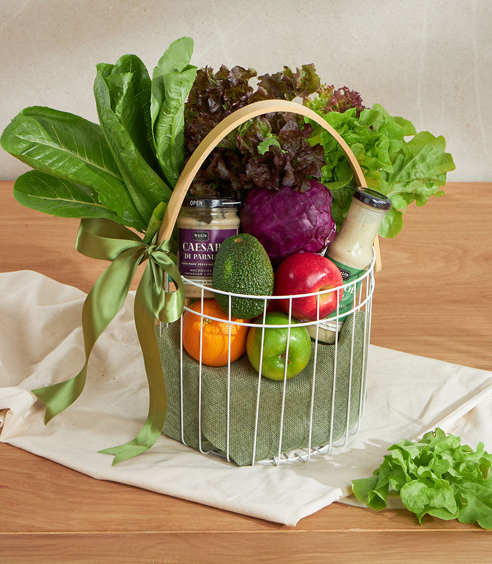 Green wellness vegetable basket with fresh lettuce, cabbage, apples, oranges, avocado and gourmet dressing