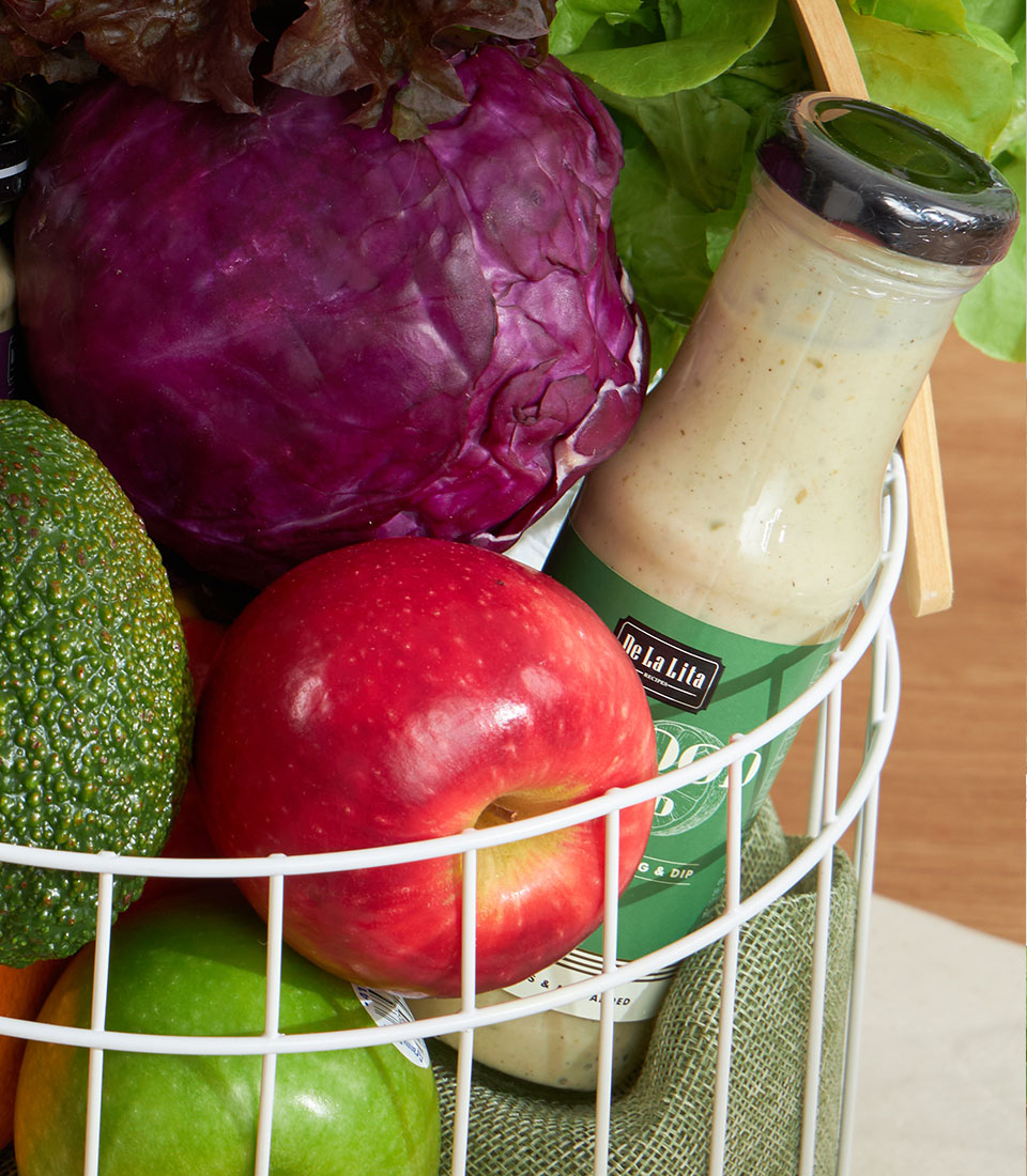 Fresh green wellness vegetable basket with avocado, cabbage, apples, and artisan dressing