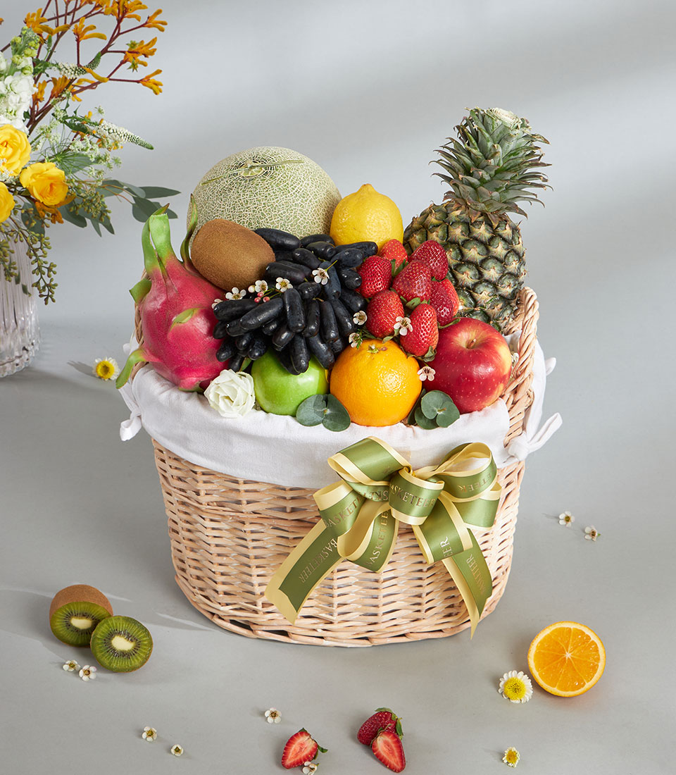 Woven wicker fruit basket with tropical cantaloupe, dragon fruit, grapes, berries, and citrus with green ribbon bow