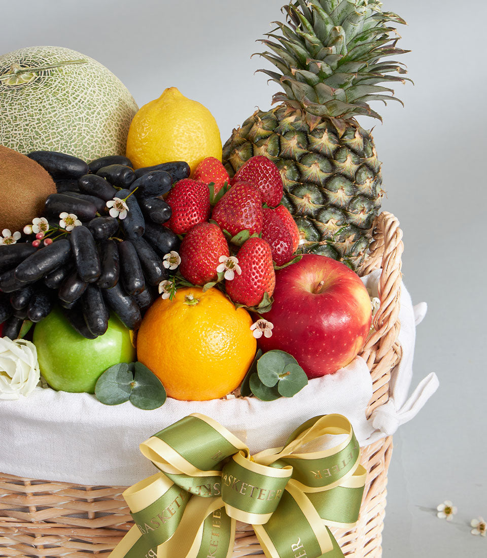Premium tropical and imported fruit basket with fresh cantaloupe, pineapple, grapes, strawberries, and citrus in woven wicker