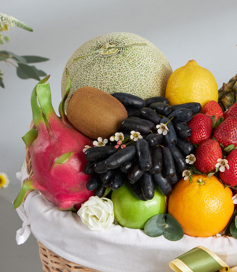 Premium tropical and imported fruit basket with cantaloupe, dragon fruit, grapes, strawberries, and fresh citrus in woven