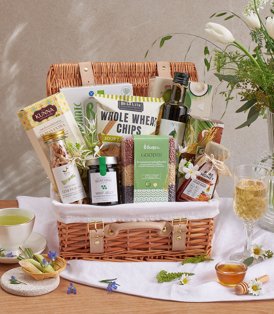Woven picnic basket wellness hamper with organic snacks, premium olive oil, honey, and herbal infusions for health-conscious