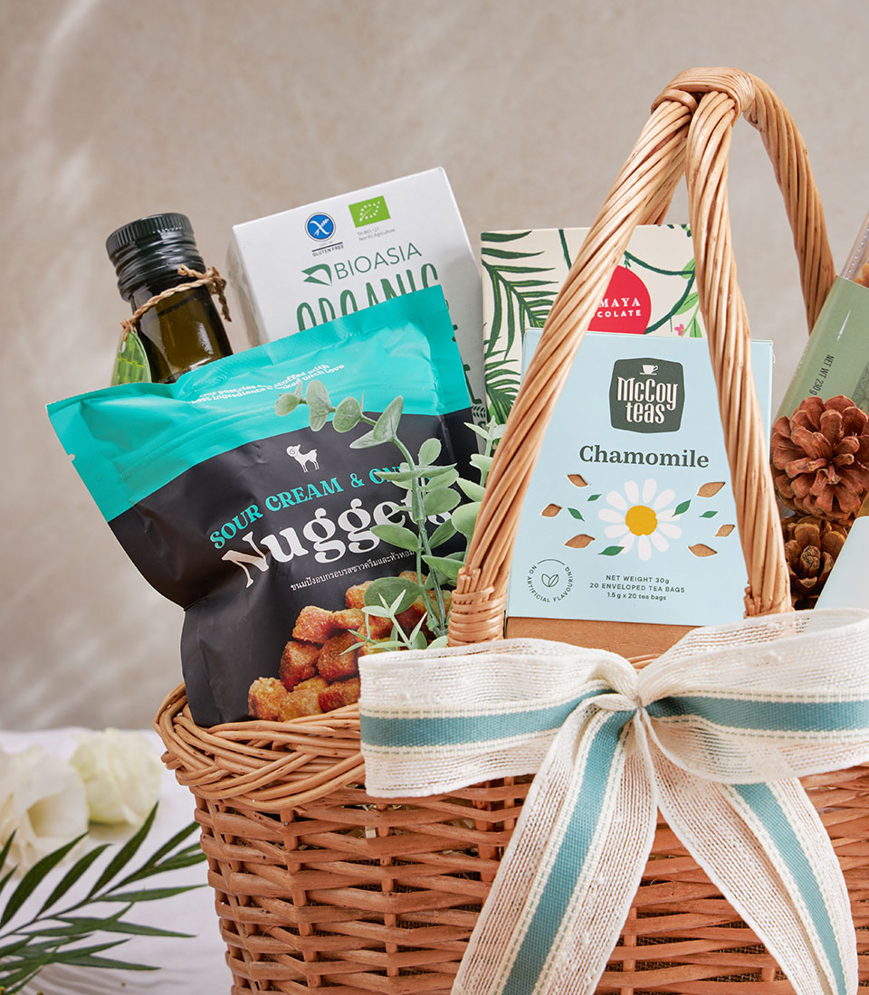 Woven wicker gift basket with premium olive oil, organic snacks, sparkling drinks, and herbal tea
