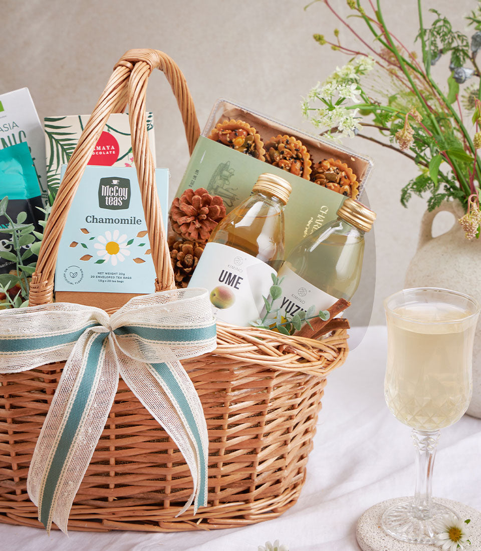 Premium wellness gift basket with olive oil, gourmet snacks, sparkling drinks and chamomile tea in woven wicker