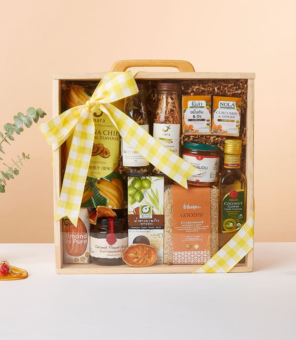 Wooden gift box filled with healthy snacks, dried fruits, tea, jams, coconut vinegar, and brown rice tied with yellow
