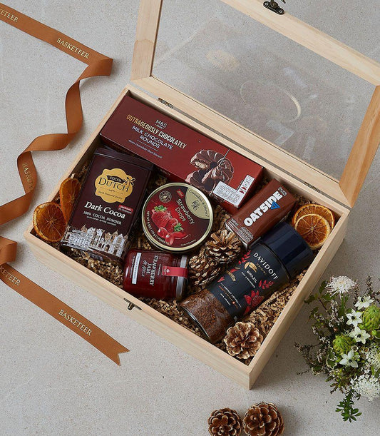 Wooden gift box filled with gourmet treats, cocoa, chocolate, jam, coffee and festive pinecones