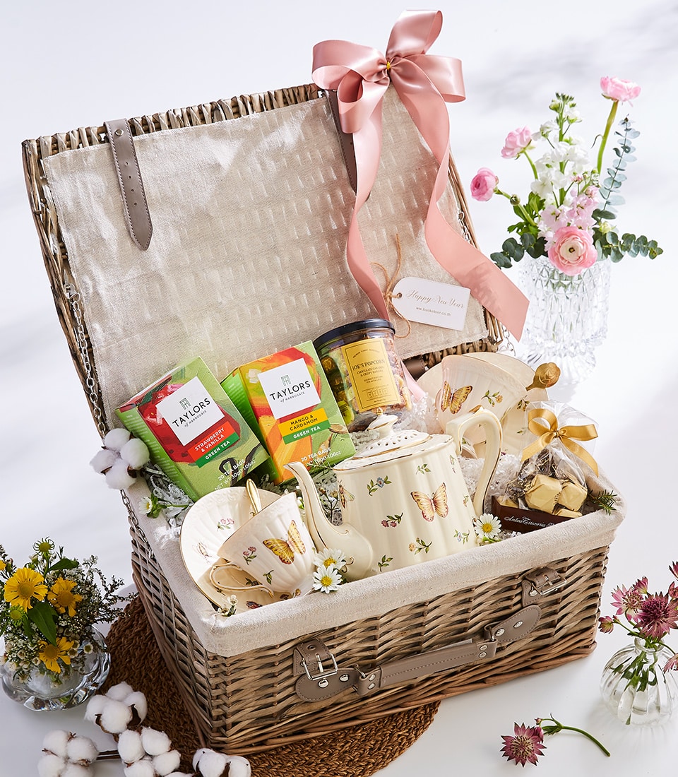 Wicker picnic hamper with premium teas, ceramic teapot, popcorn, and fresh flowers for gifting