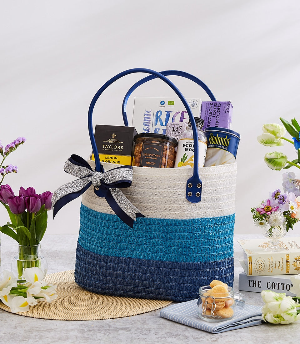 Woven tote gift bag with blue and white sections filled with gourmet treats and tea for New Year gifting