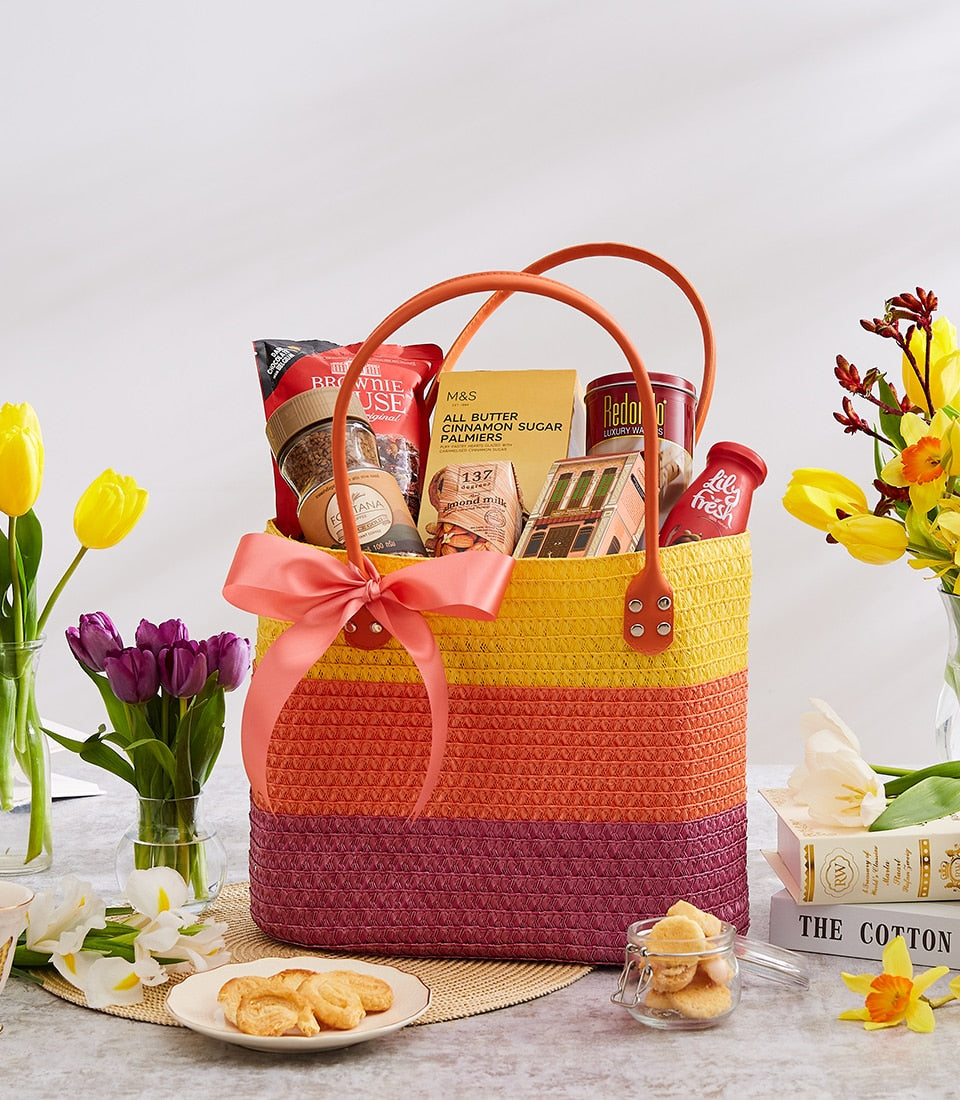 Colorful striped woven gift basket with gourmet treats, coffee, and pastries, tied with peachy-pink ribbon