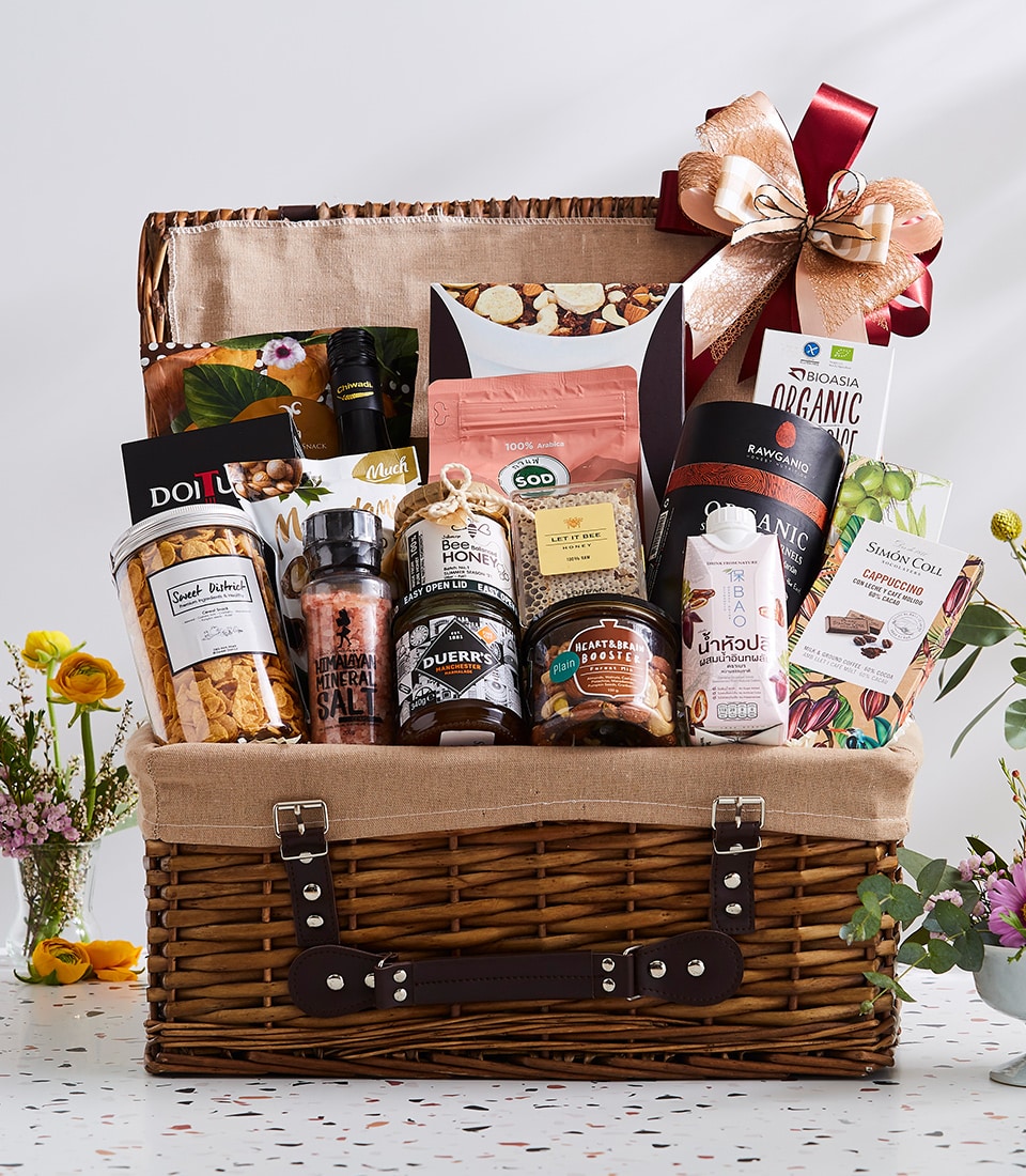 Large wicker picnic basket filled with gourmet foods, honey, nuts, cereals, and organic goods with gold and red ribbon bow