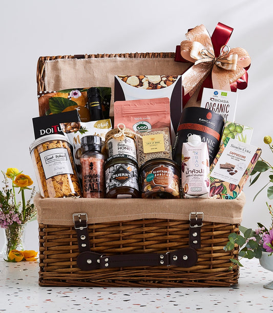 Large wicker picnic basket filled with gourmet foods, honey, nuts, cereals, and organic goods with gold and red ribbon bow