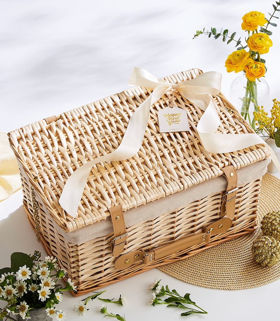 Wicker picnic basket with beige lining, cream satin bow, and Happy New Year gift tag, surrounded by yellow flowers and gold