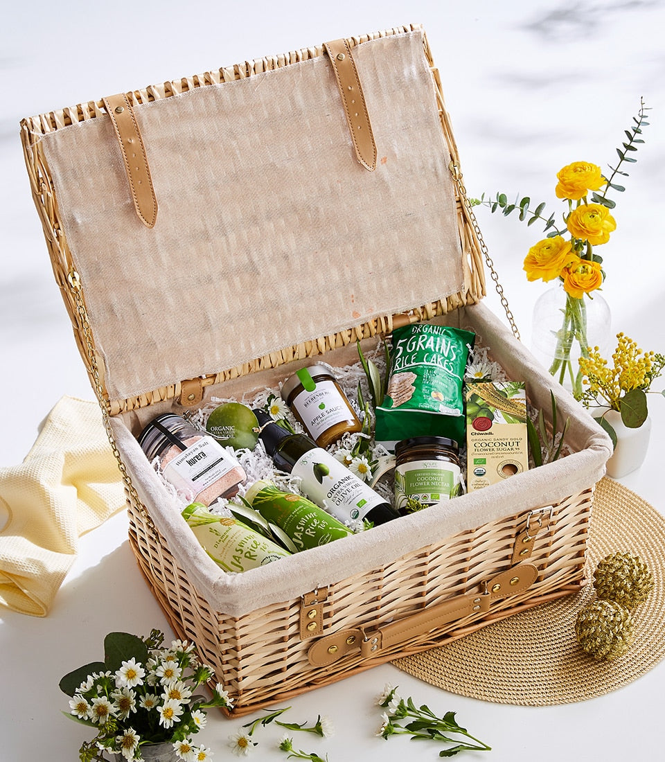 Wicker picnic basket filled with organic wellness foods, himalayan salt, olive oil, and herbal tea with white daisies