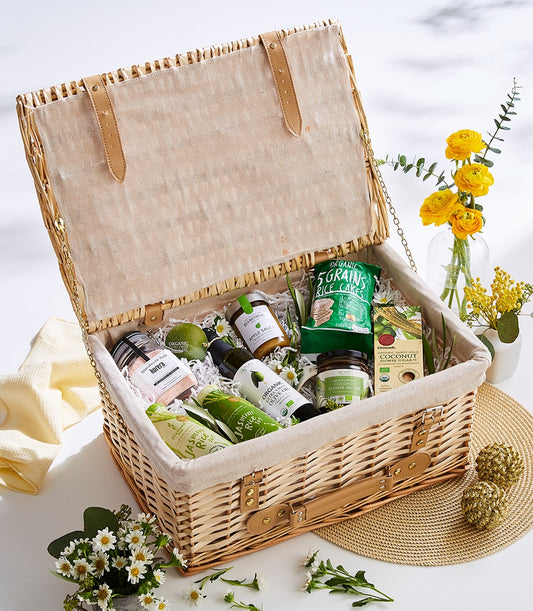 Wicker picnic basket filled with organic wellness foods, himalayan salt, olive oil, and herbal tea with white daisies