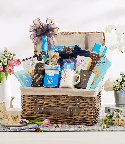 Wicker gourmet hamper with sparkling beverage, biscuits, chocolate, coffee and marble mug tied with grey ribbon
