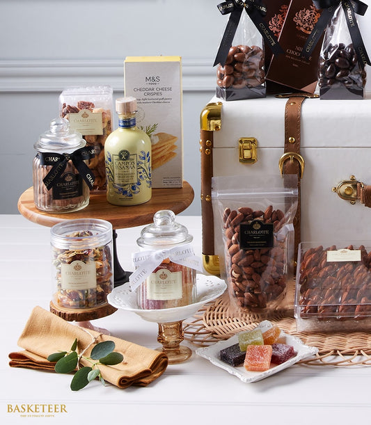 Elegant gourmet gift hamper with champagne, chocolate-covered nuts, artisan cheeses, and luxe accessories in white