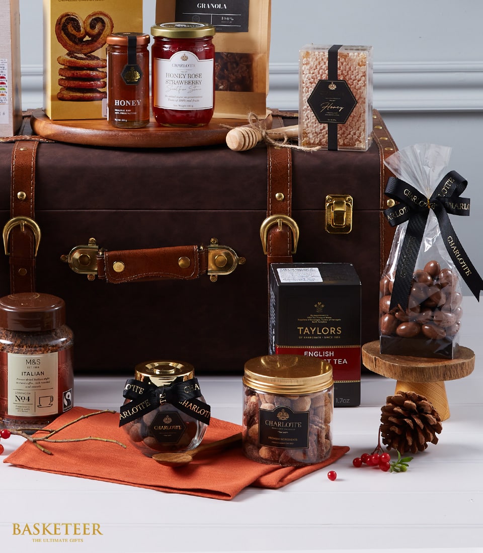 Luxury gourmet hamper with chocolates, honey, jam, coffee, tea, and nuts arranged on leather trunk