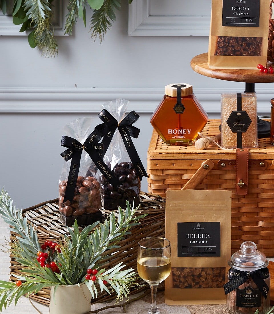 Luxury gourmet hamper with honey, granola, chocolate-covered nuts, and fine wine accessories in wicker basket