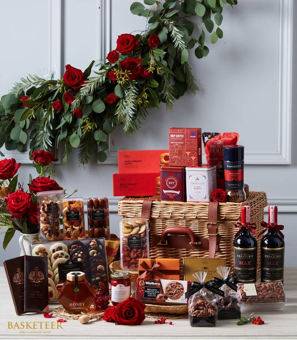 Luxury wine hamper with red wines, gourmet chocolates, nuts, honey, and artisan treats in wicker basket with roses