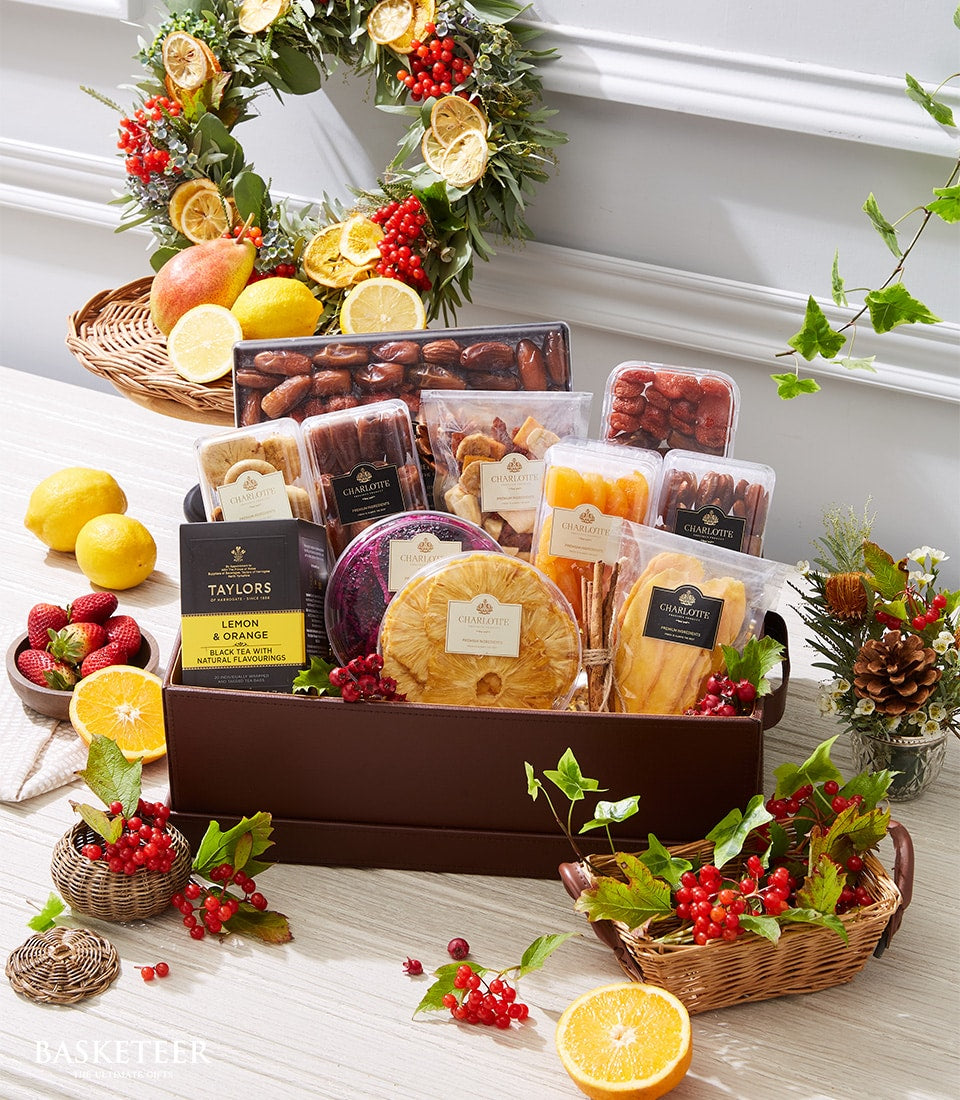 Luxury gourmet gift basket with dried fruits, nuts, premium tea, and fresh citrus on wooden surface